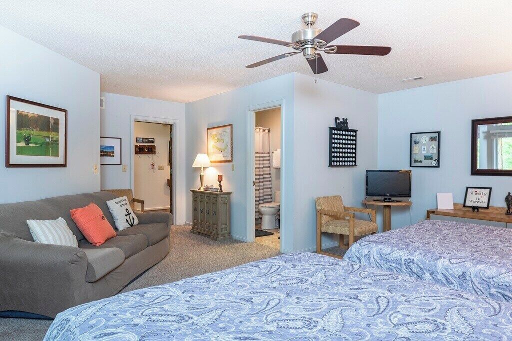 A bedroom with a bed, a sofa, a television, and a ceiling fan.