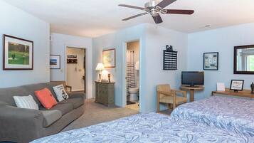 A bedroom with a bed, a sofa, a television, and a ceiling fan.