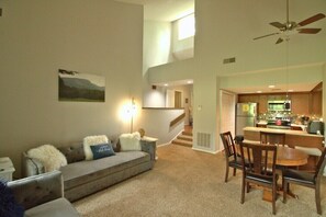 A living room with a sofa, a dining table with chairs, a kitchen area, and a staircase. - Fairway Villa 1504 at Rumbling Bald (Lake Lure)