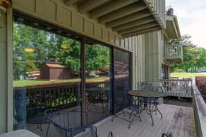 Eine überdachte Terrasse im Freien mit Tisch und Stühlen, ein Holzdeck und Blick auf einen Garten mit Gartenhaus und Bäumen.