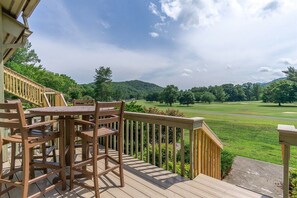 A wooden deck with a table and chairs, overlooking a golf course.