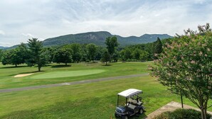A golf course with a golf cart, trees, and mountains in the background. - Fairway Villa 502 at Rumbling Bald (Lake Lure)