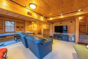 A log cabin interior with a sofa, table, television, and fireplace.