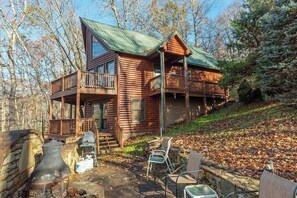 A log cabin with a balcony, outdoor seating, and a stone fireplace.