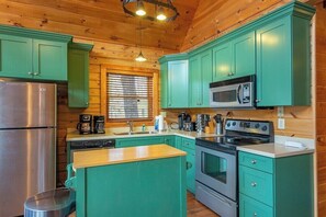 A compact kitchen with green cabinets, a stainless steel refrigerator, a microwave, and a stove.