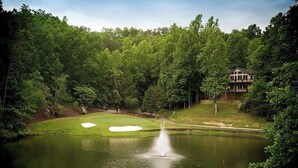 Un étang paisible avec une fontaine, entouré d’une végétation luxuriante et d’un terrain de golf.