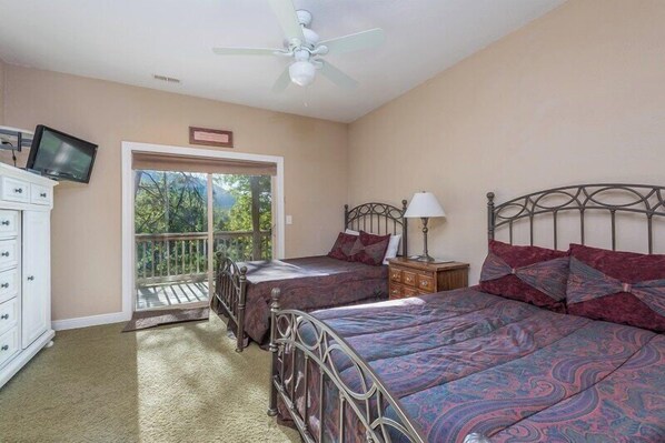 Une chambre avec deux lits, un ventilateur de plafond, une télévision, une commode et un balcon.