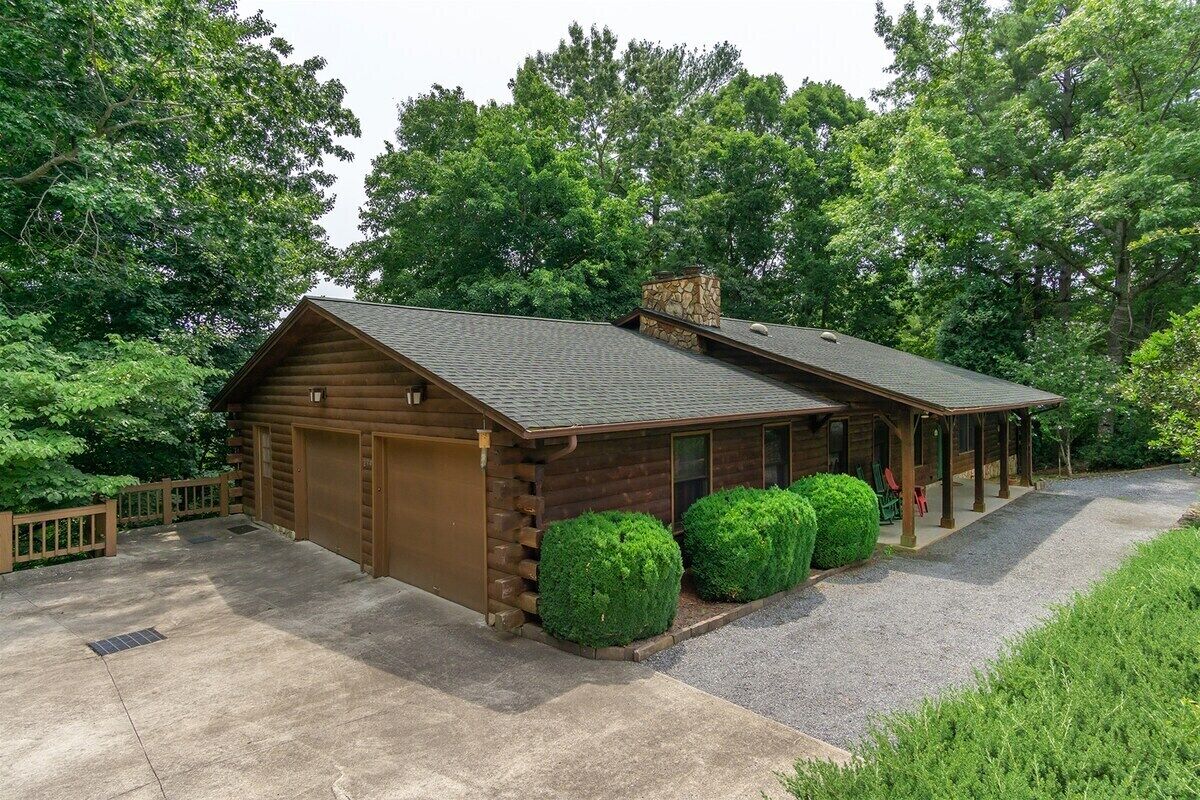 Une cabane en rondins avec un garage, une véranda et un jardin bien entretenu.