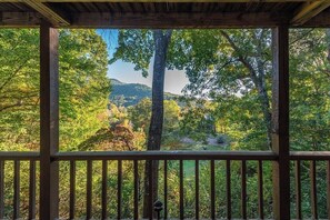 A wooden deck with a view of a forested area and hills. - Relaxation Station at Rumbling Bald (Lake Lure)
