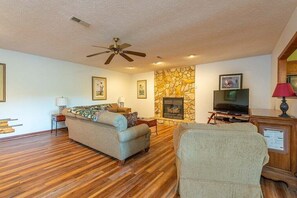 A living room with a fireplace, a television, and a ceiling fan.