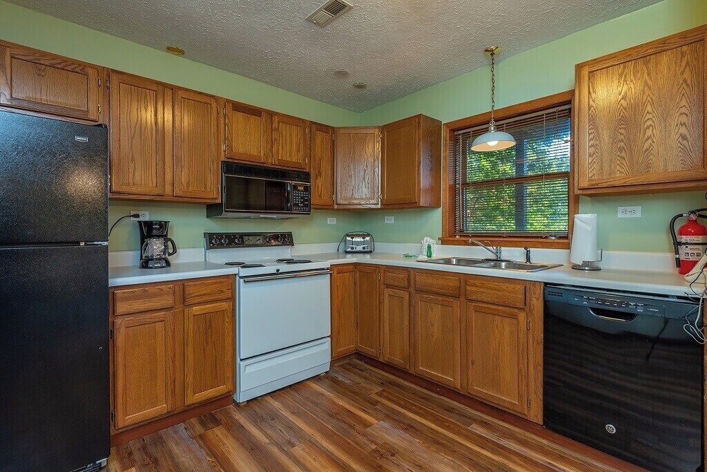 A kitchen with wooden cabinets, a black refrigerator, a white stove, a microwave, a toaster, and a dishwasher.