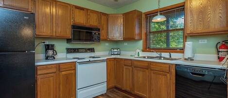 A kitchen with wooden cabinets, a black refrigerator, a white stove, a microwave, a toaster, and a dishwasher.