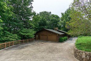 A log cabin with two garage doors, surrounded by a stone retaining wall and a wooden fence.