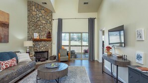 A spacious living room with a stone fireplace, a sofa, a coffee table, and a TV mounted on the wall.