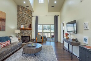 A spacious living room with a stone fireplace, a sofa, a coffee table, and a TV mounted on the wall.