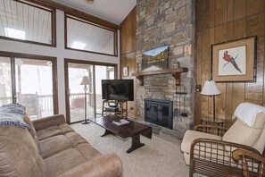 A living room with a stone fireplace, a television, and a large window.