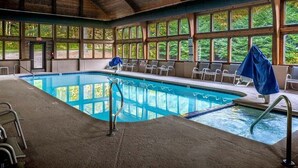 Une piscine intérieure dotée d’un plafond en bois, de grandes fenêtres et de chaises longues.