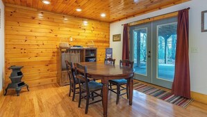 Un intérieur en bois comprenant une table à manger, des chaises, un poêle et une vue à travers des portes vitrées.