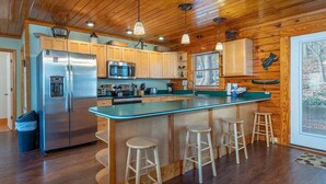 A kitchen with wooden cabinets, a stainless steel refrigerator, a microwave, and a large island with stools.