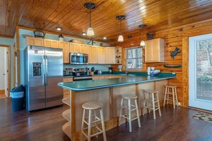 A kitchen with wooden cabinets, a stainless steel refrigerator, a microwave, and a large island with stools.