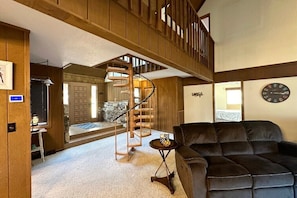 A spacious living area with a large black leather sofa, a wooden staircase, and a stone fireplace. - Tranquility at Rumbling Bald (Lake Lure)