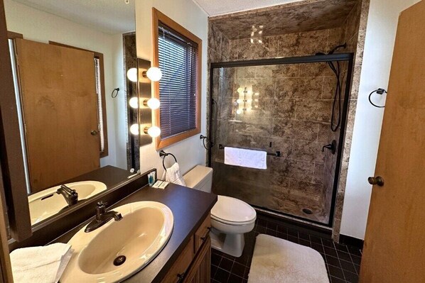 A bathroom with a large mirror, two sinks, a toilet, and a glass-enclosed shower.