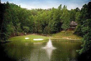 A serene pond with a fountain, surrounded by lush greenery and a golf course. - Tranquility at Rumbling Bald (Lake Lure)
