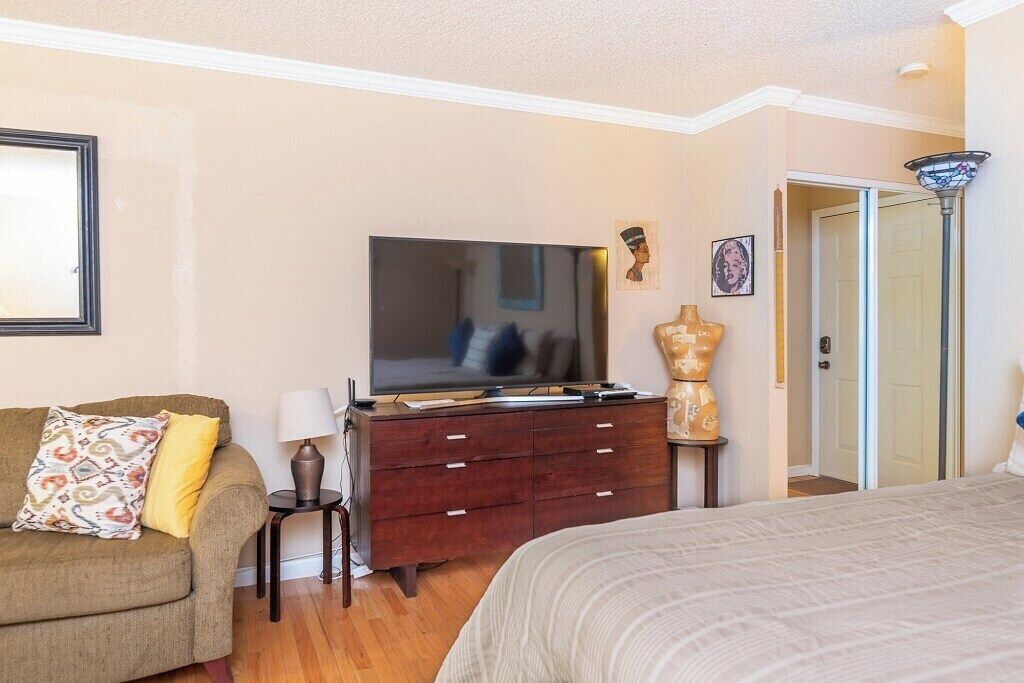 A bedroom with a bed, a dresser, a television, a lamp, and a door.
