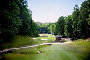 A golf course with a pond, a bridge, and a pavilion.