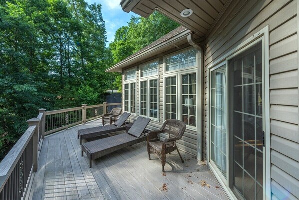 A wooden deck with outdoor furniture, large windows, and a view of a wooded area.
