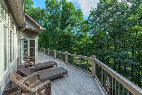 A wooden deck with wicker furniture, surrounded by trees.