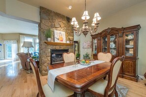 A dining room with a stone wall, chandelier, wooden cabinet, and a fireplace.