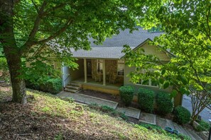 A house with a porch, steps leading to the entrance, and a garden with various plants and a tree.