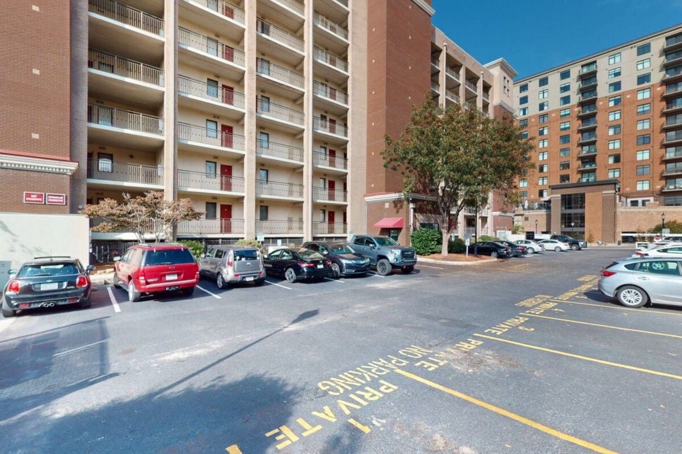 A multi-story parking garage with several cars parked, a clear sky, and a building with balconies in the background.