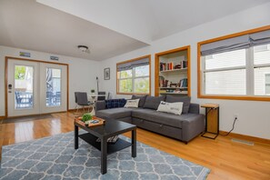 A living room with a sectional sofa, a coffee table, a bookshelf, and a dining area with chairs.