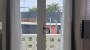 A room with a sliding glass door leading to an outdoor balcony. The balcony has a white railing and a view of a building with a McDonald's sign. - T1 apartment in the city center of Grand-Baie 2 minutes from the beach (Grand Baie)