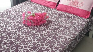 A bed with a patterned bedspread, two pillows with floral designs, and a bouquet of pink flowers on the bed. - T1 apartment in the city center of Grand-Baie 2 minutes from the beach (Grand Baie)