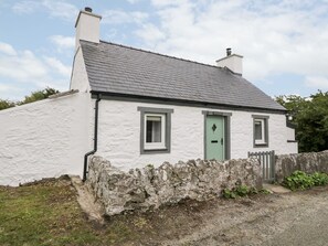 A white cottage with a grey roof, a green door, and a stone wall in front. - Rhytty Bach (Ty Croes)