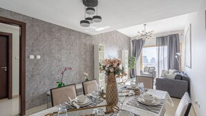 Een eethoek met een lange tafel voor vier personen, een vaas met bloemen en stadszicht door grote ramen.