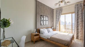 Een moderne slaapkamer met een groot bed, een glazen tafel met een vaas, een stoel en uitzicht op de stad door grote ramen.