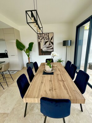A modern dining area with a wooden table, blue chairs, potted plants, and a contemporary light fixture. - Villa Beauregard center Uzès with view on the heure valley and swimming pool (uzes)