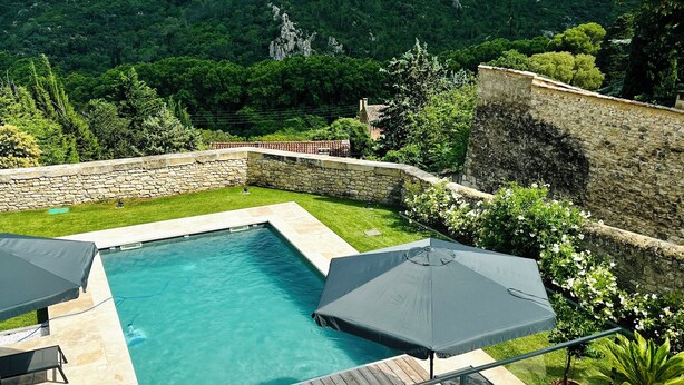 Une piscine bordée d’un mur en pierre, avec vue sur une colline boisée.