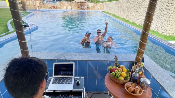Un área de piscina con una computadora portátil sobre una mesa, un frutero y una bebida al borde de la piscina.