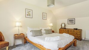 A bedroom with a wooden bed, two bedside tables with lamps, a wooden dresser, and framed pictures on the walls.