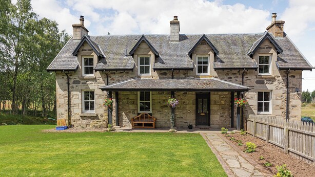 A stone house with a stone porch, multiple chimneys, and a well-maintained lawn.