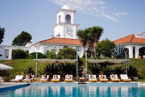 A pool area with lounge chairs and a building with a bell tower in the background. - Posada del Qenti (Villa Icho Cruz)