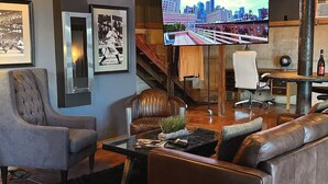 A modern living room with a leather sofa, a glass coffee table, a leather armchair, and a television mounted on the wall displaying a cityscape. - Amazing view and location (Springfield)