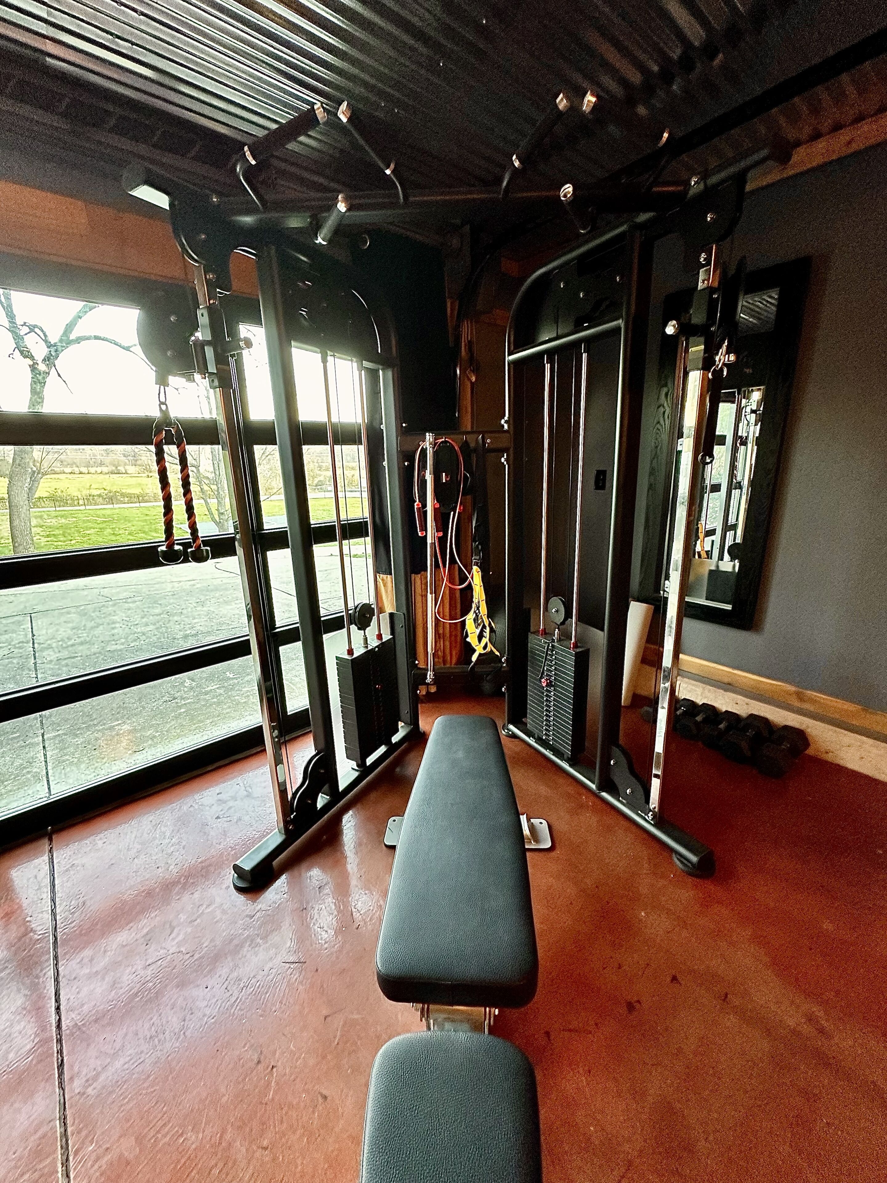 Ein Fitnessstudio mit einer Bank, Kraftgeräten und einem großen Fenster.