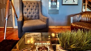 A cozy living room with a tufted armchair, a leather sofa, and a glass coffee table displaying a Star Wars magazine. - Amazing view and location (Springfield)