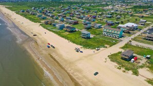 Ett flygbildsbild av ett bostadsområde vid kusten, med hus längs stranden och en stor, blå byggnad med en unik design.